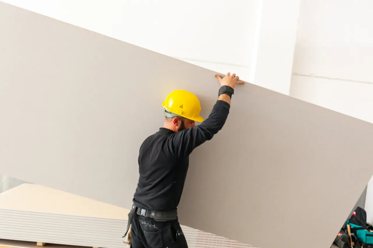 Construction worker carrying drywall sheet in Massachusetts