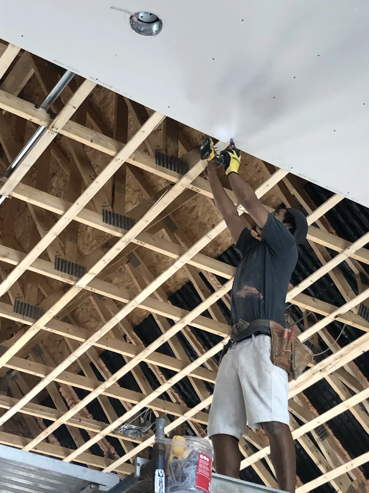 Crew member fastening ceiling drywall to exposed joists in a Massachusetts home