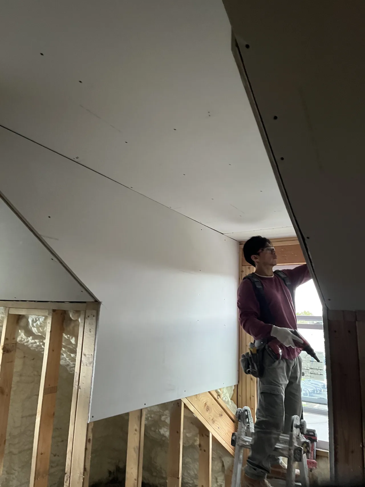 Crew member hanging drywall board on a sloped ceiling in a Massachusetts home